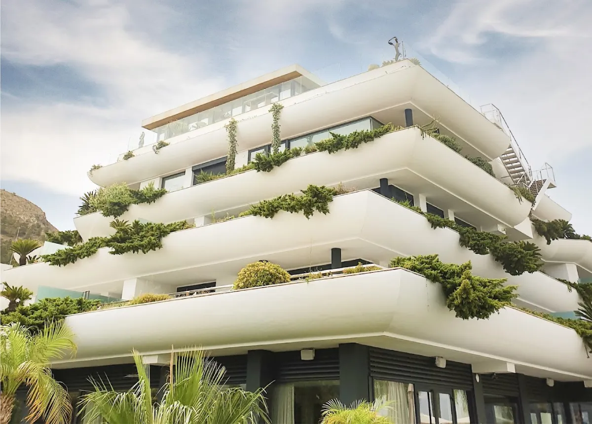 Modern luxury hotel with balcony views surrounded by trees under a clear summer sky