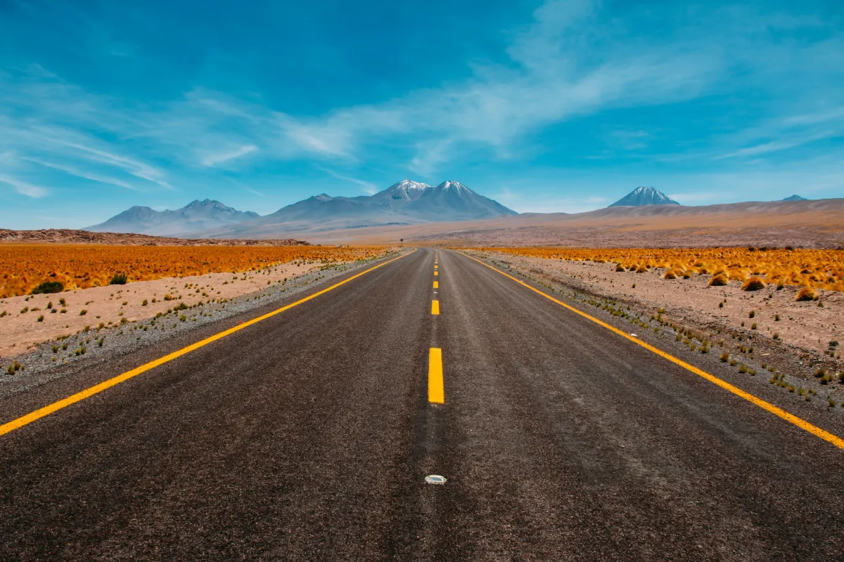 Empty asphalt road in a remote desert landscape with mountains under a daylight sky.