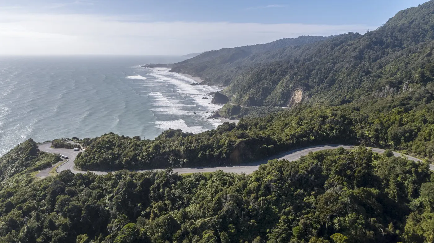Scenic daytime view of tranquil sea by the island with mountains, tree-lined seashore and open sky
