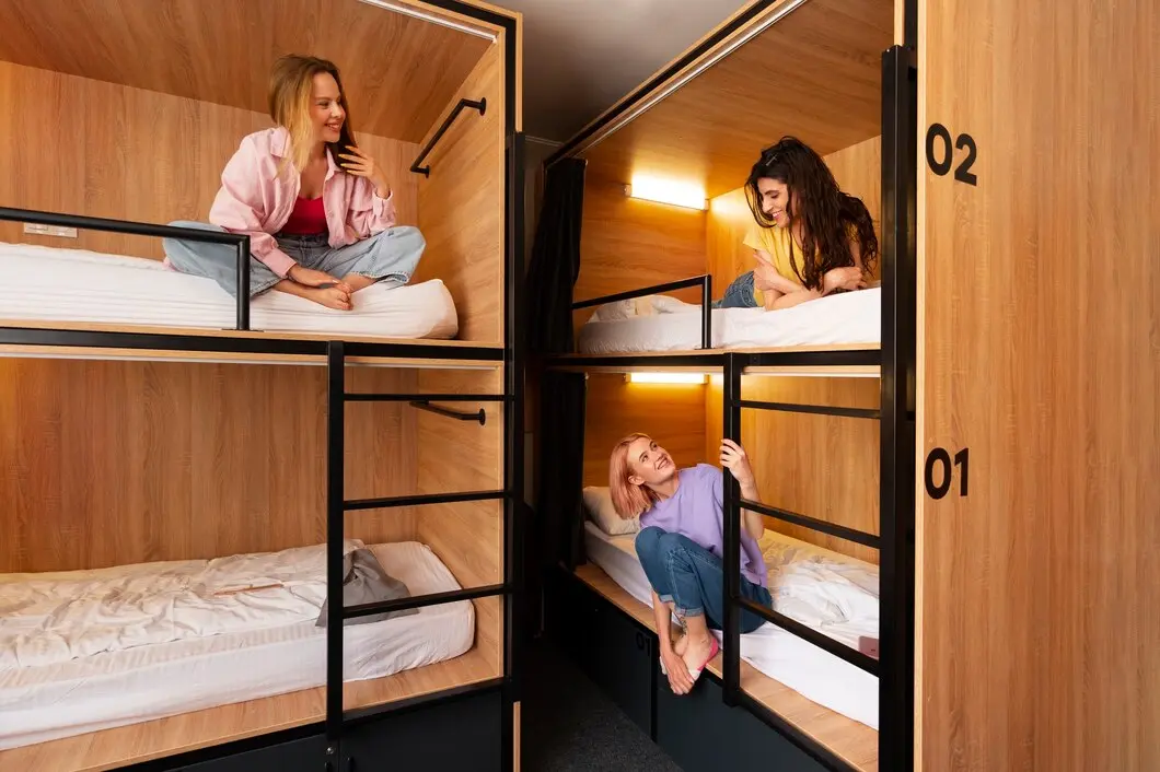 Three women relax in modern bunk beds with wooden panels, engaged in conversation in a cozy, shared accommodation space.