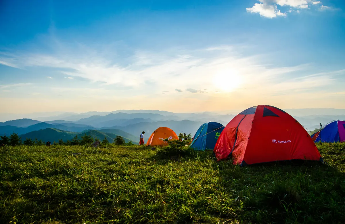 Sunset over a tent in a grassy mountain landscape during a summer travel adventure