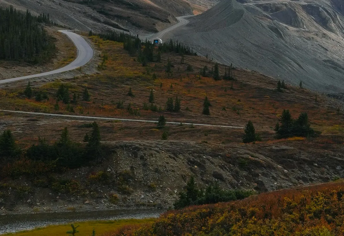 Scenic daylight view of a valley with a road running through, surrounded by mountains, trees, cropland and a river.