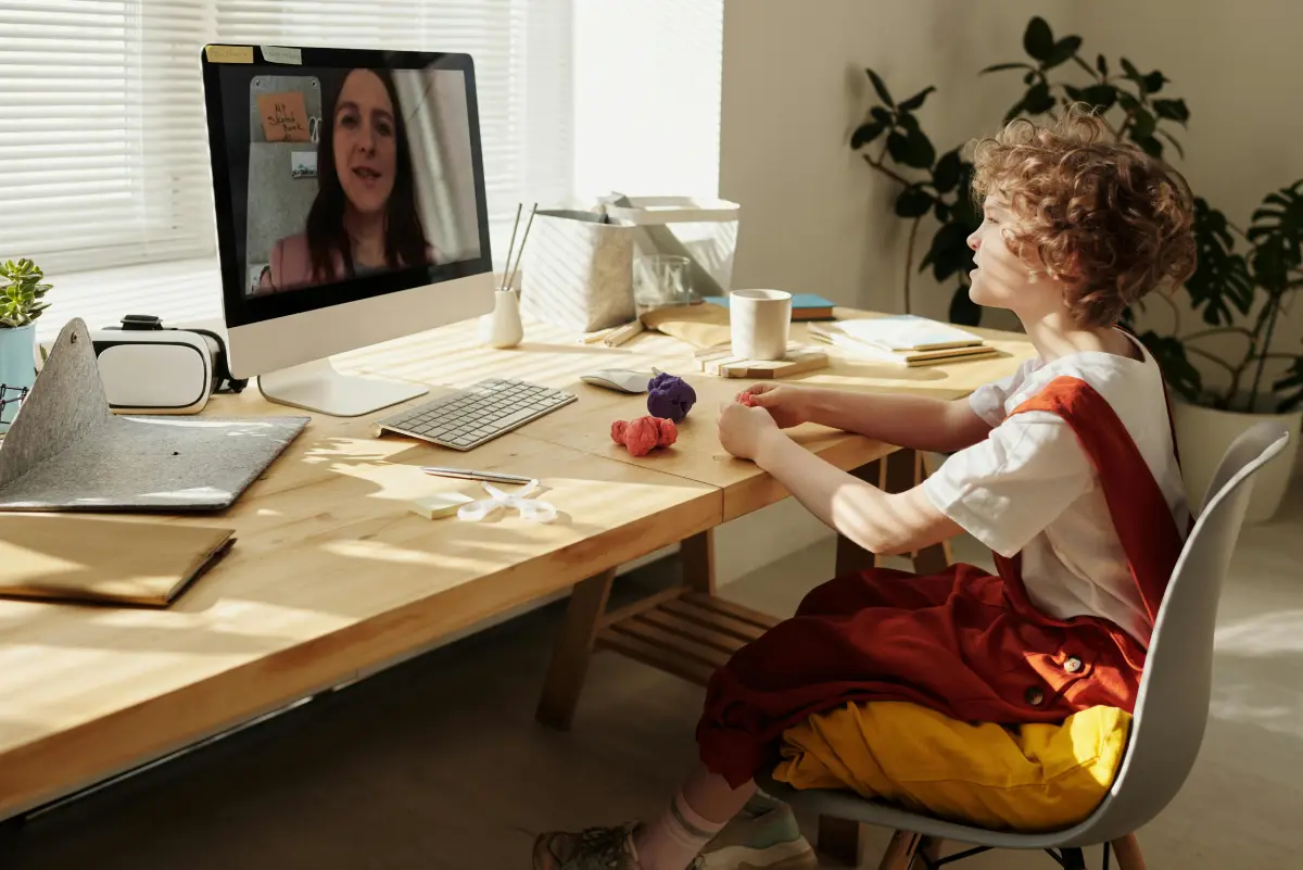 Adult woman and child sitting at a desk, using laptop for online education in a family room