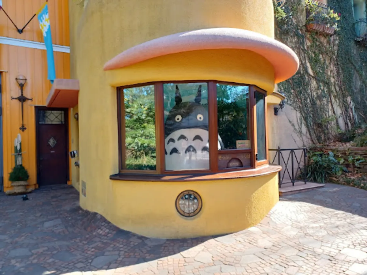 A whimsical yellow building features a round window displaying a large Totoro figure.