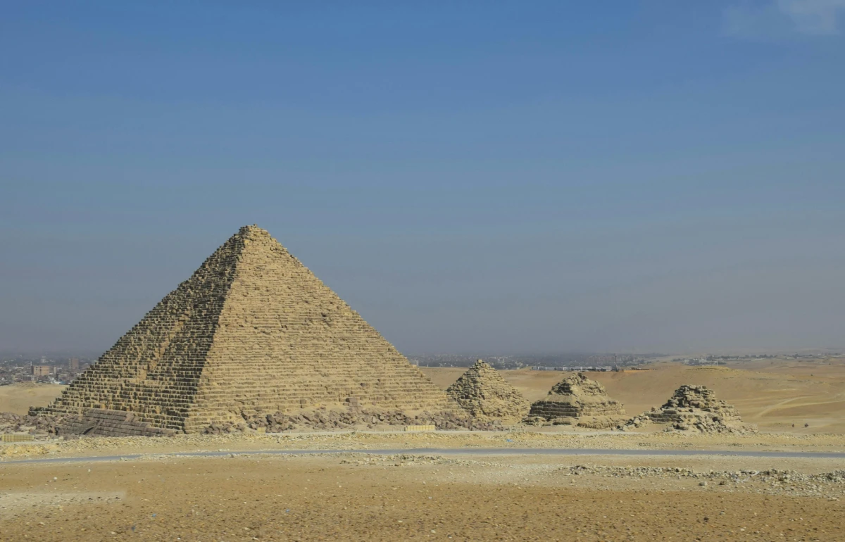 Camels navigating across arid desert landscape with ancient pyramids under the summer sun