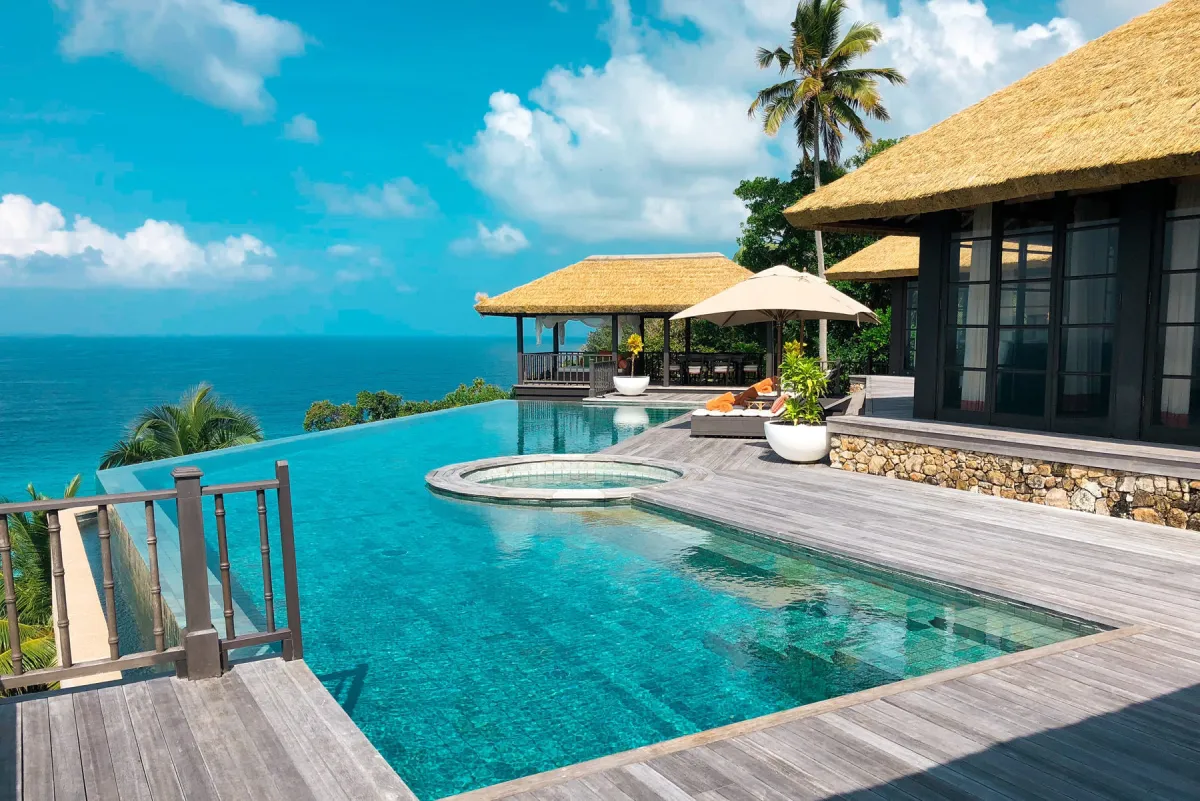 Luxury villa hotel with a dug-out swimming pool, patio chairs and umbrella for a tropical summer vacation.