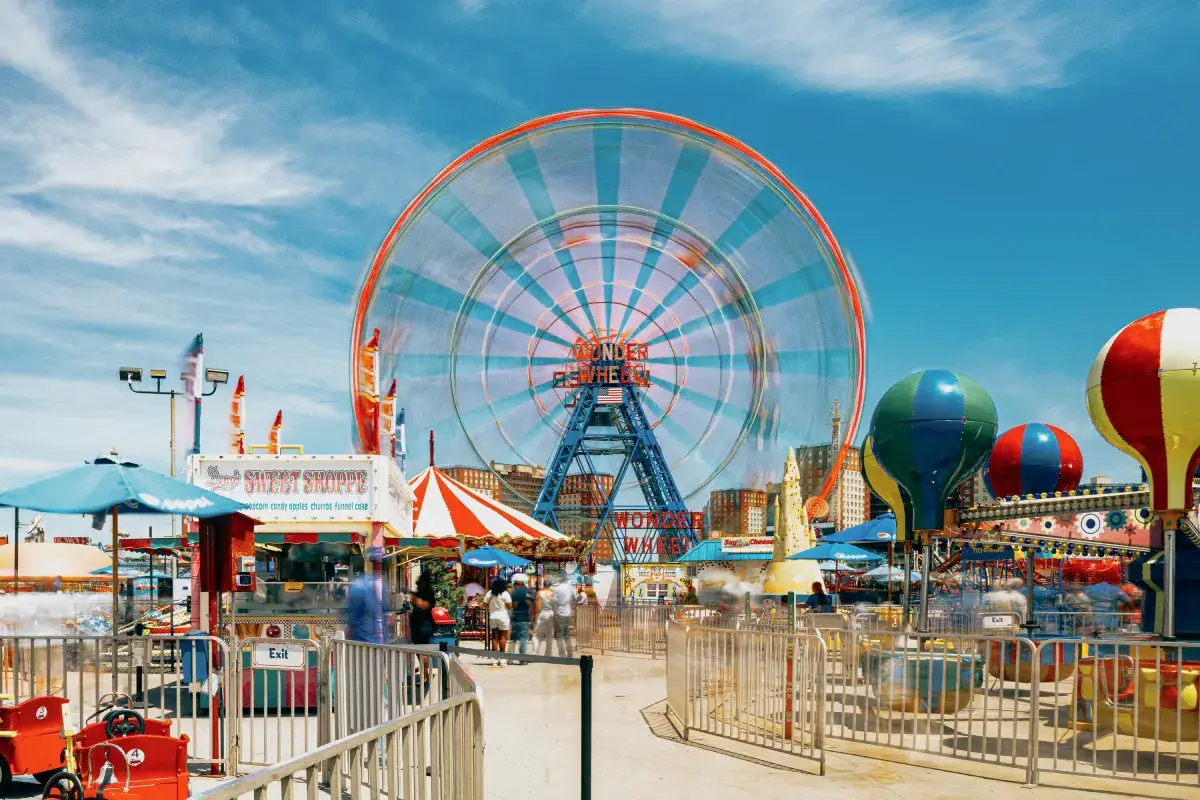 A vibrant amusement park scene featuring a colorful Ferris wheel against a clear blue sky, with excited visitors and attractions around.