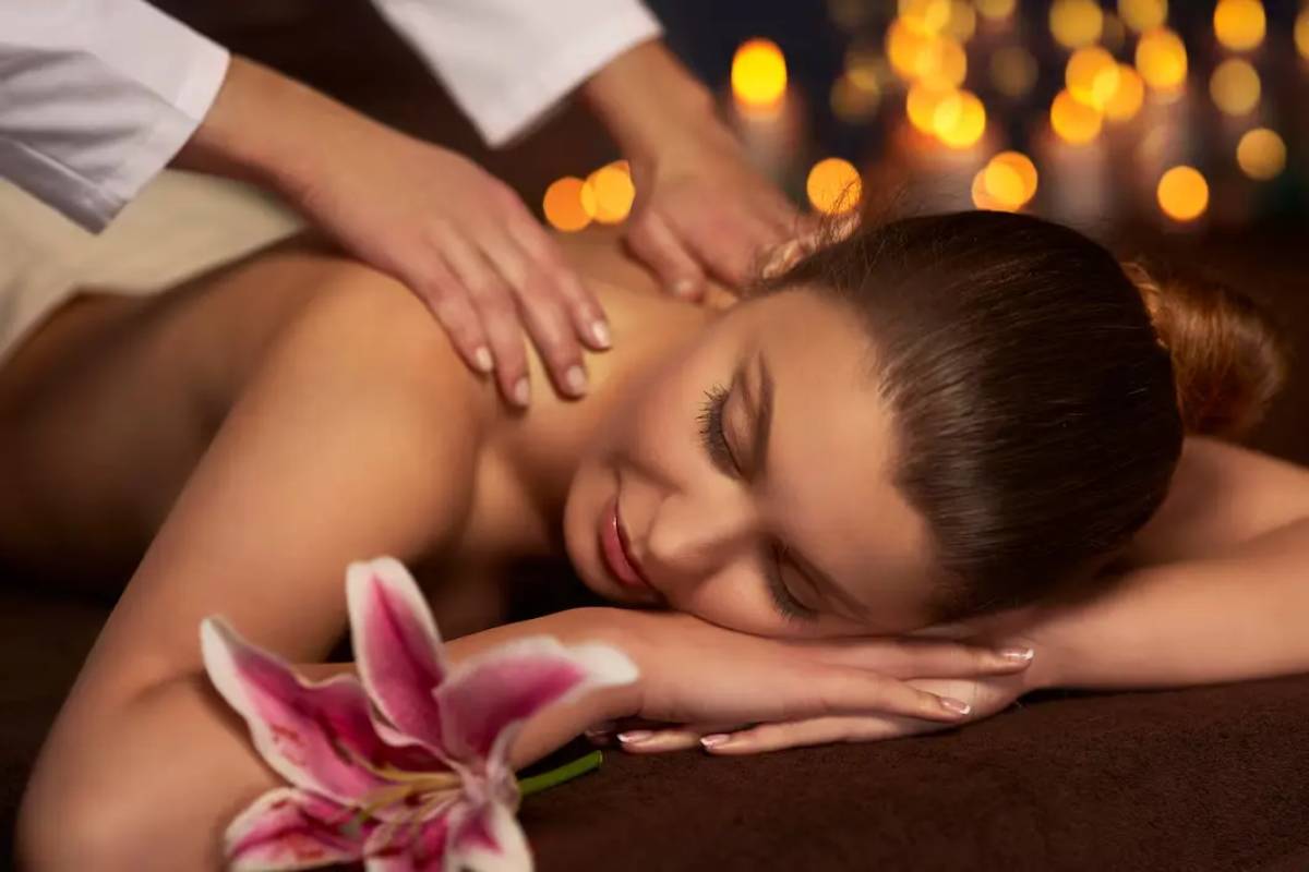 A relaxing spa featuring a woman receiving a massage, surrounded by candles and a pink lily flower.