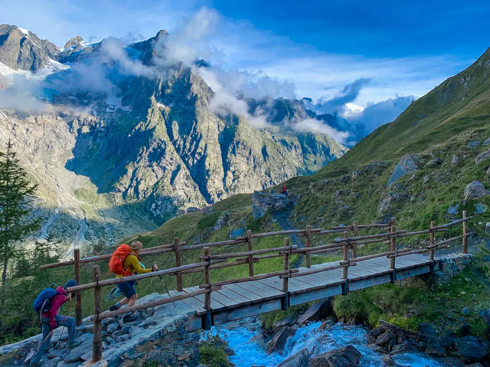 Scenic summer view of a hiker advancing towards a snow-topped mountain peak, overlooking a sparkling lake